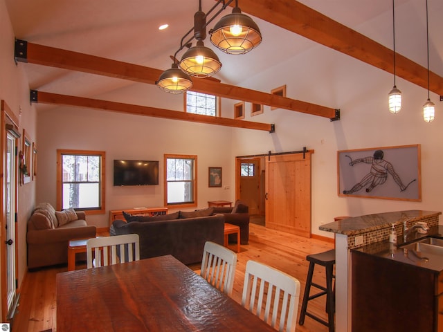 dining area featuring a barn door, sink, vaulted ceiling with beams, and light hardwood / wood-style flooring