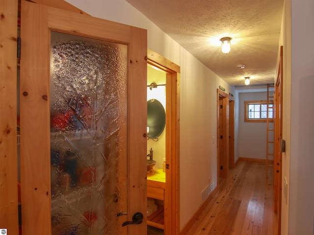 corridor featuring a textured ceiling and light hardwood / wood-style floors