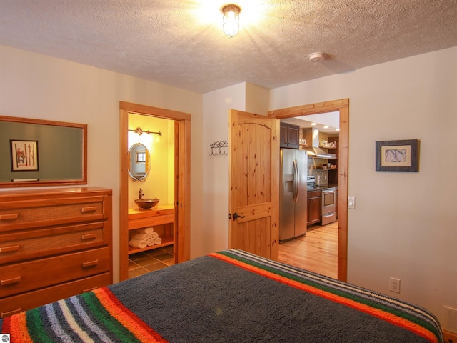 bedroom featuring ensuite bath, light hardwood / wood-style flooring, a textured ceiling, and stainless steel fridge with ice dispenser