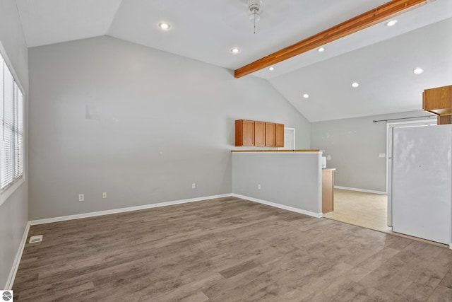 unfurnished living room featuring vaulted ceiling with beams and light wood-type flooring