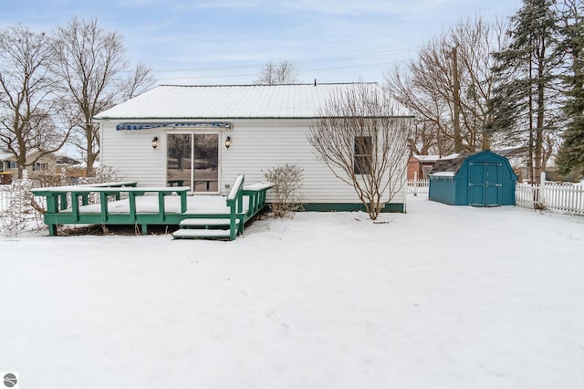 snow covered rear of property with a wooden deck and a storage unit