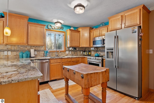 kitchen featuring sink, decorative light fixtures, light wood-type flooring, appliances with stainless steel finishes, and light stone countertops