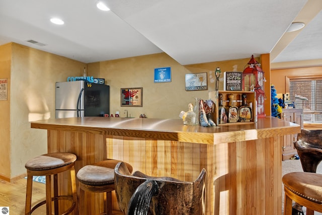 bar with stainless steel refrigerator and light hardwood / wood-style floors