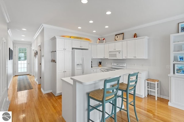 kitchen featuring white appliances, light hardwood / wood-style floors, white cabinets, and a kitchen bar