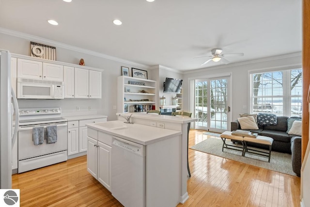 kitchen featuring white cabinets, ornamental molding, light hardwood / wood-style floors, a center island with sink, and white appliances