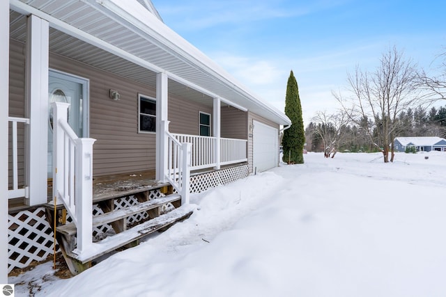 snow covered property entrance featuring a garage and a porch