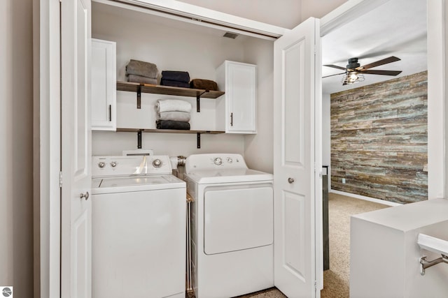 clothes washing area featuring cabinets, ceiling fan, washer and clothes dryer, and wood walls