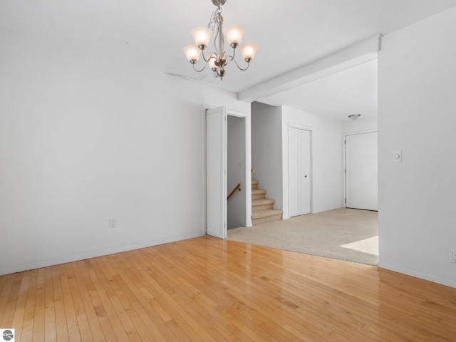 empty room with beam ceiling, a chandelier, and light hardwood / wood-style floors