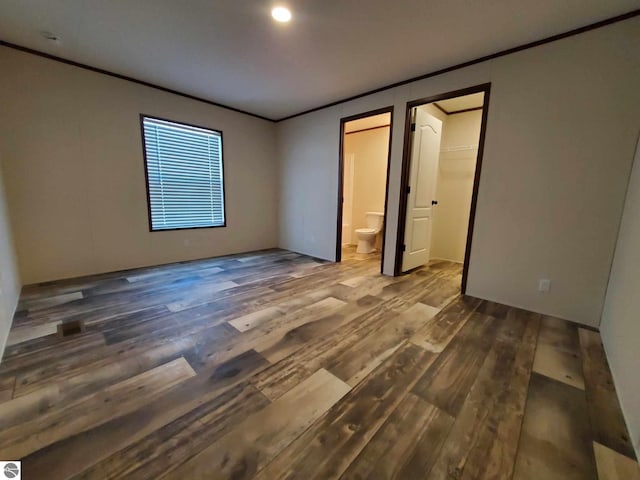 unfurnished bedroom featuring a walk in closet, ensuite bath, dark wood-type flooring, and ornamental molding