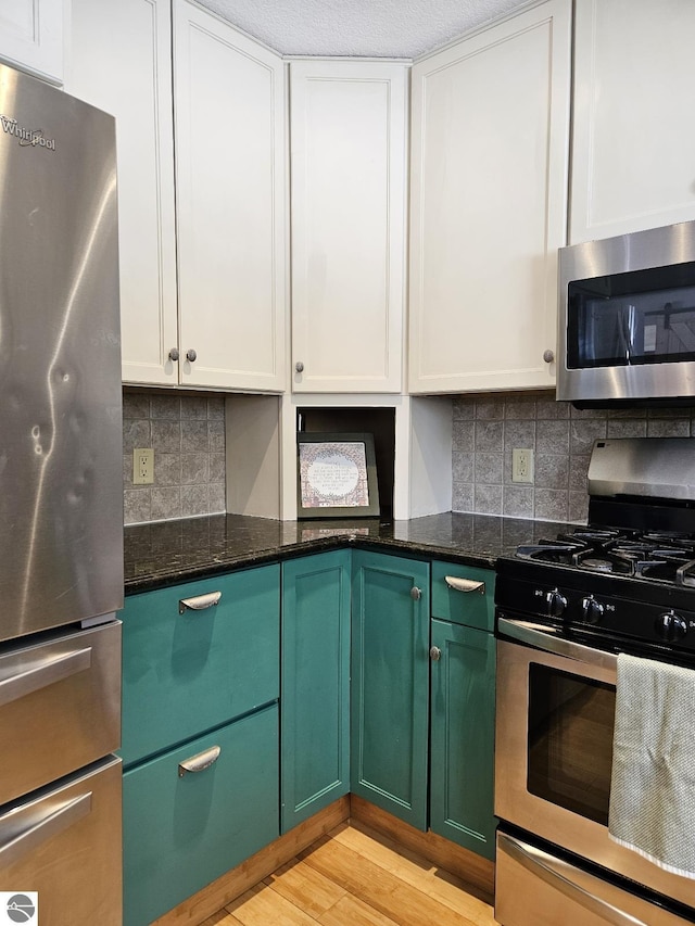 kitchen featuring tasteful backsplash, appliances with stainless steel finishes, dark stone counters, light hardwood / wood-style floors, and white cabinets