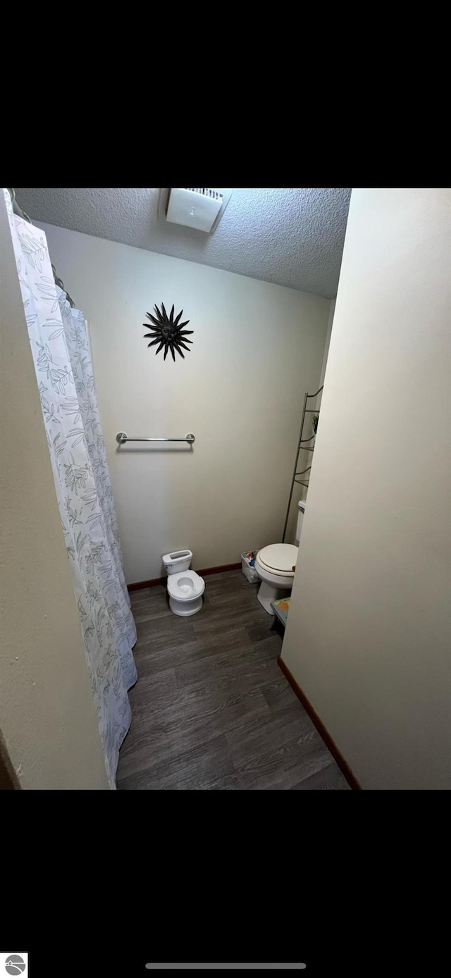 bathroom featuring a shower with curtain, wood-type flooring, toilet, and a textured ceiling