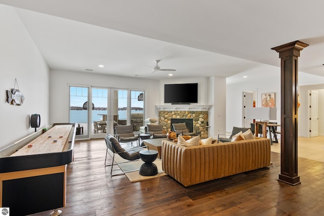 living room with ceiling fan, dark wood-type flooring, decorative columns, and a stone fireplace