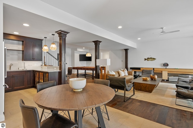 dining room with light wood-type flooring, ceiling fan, decorative columns, and sink