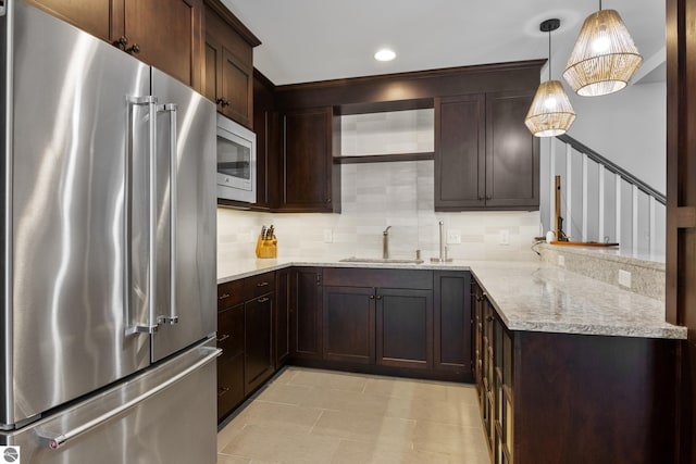 kitchen featuring stainless steel appliances, dark brown cabinetry, light stone counters, pendant lighting, and sink