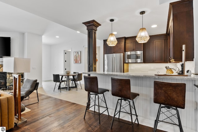 kitchen with a breakfast bar, light wood-type flooring, pendant lighting, stainless steel appliances, and dark brown cabinetry