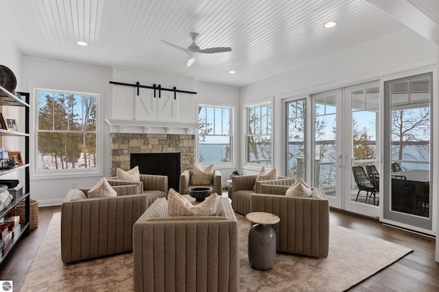 interior space with a healthy amount of sunlight, ceiling fan, a stone fireplace, and dark hardwood / wood-style floors