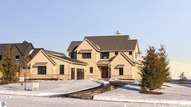 view of front of house with stone siding, a shingled roof, a chimney, and board and batten siding