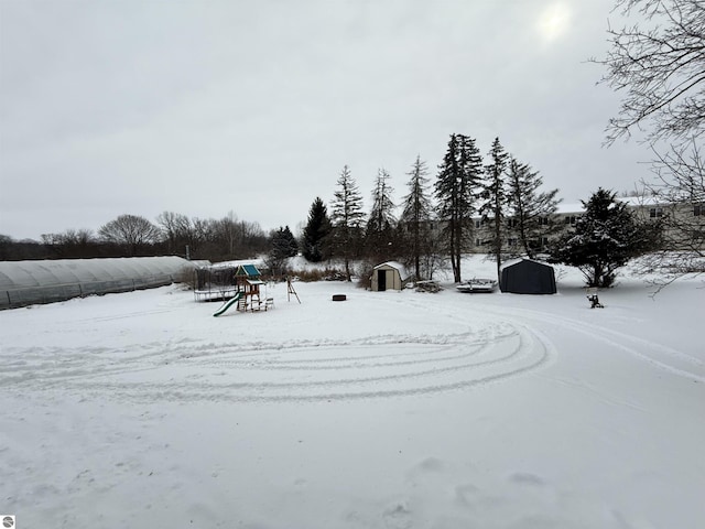 yard layered in snow featuring a playground and a shed