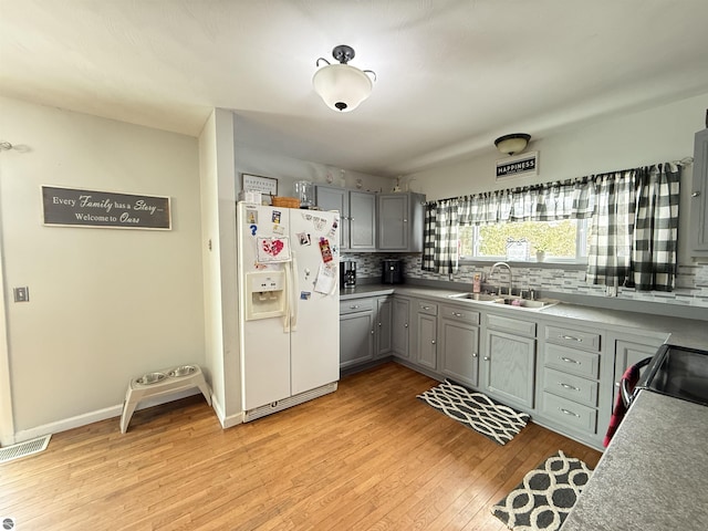 kitchen featuring tasteful backsplash, sink, gray cabinetry, white fridge with ice dispenser, and light wood-type flooring