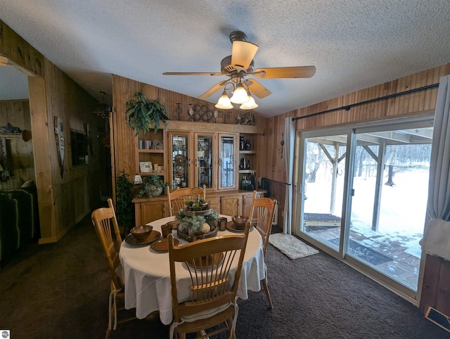 dining space with ceiling fan, dark carpet, a textured ceiling, and wood walls