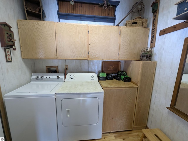 clothes washing area with cabinets, washer and clothes dryer, and light wood-type flooring