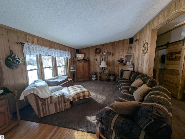 living room with vaulted ceiling, a textured ceiling, wooden walls, hardwood / wood-style flooring, and a barn door