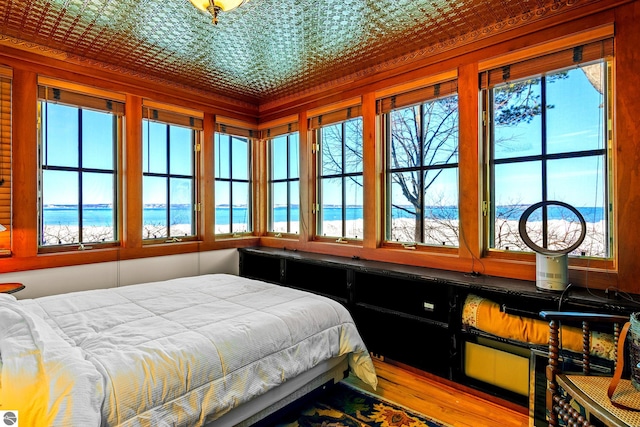 bedroom featuring multiple windows, crown molding, hardwood / wood-style flooring, and a water view