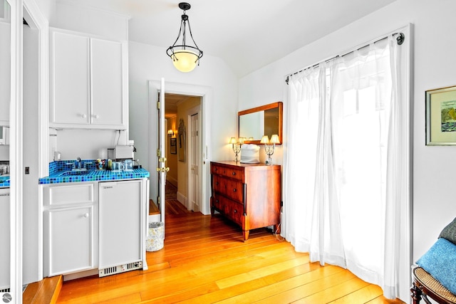 kitchen featuring sink, decorative light fixtures, light wood-type flooring, fridge, and white cabinets