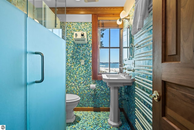 bathroom featuring tile walls, toilet, and a shower with door