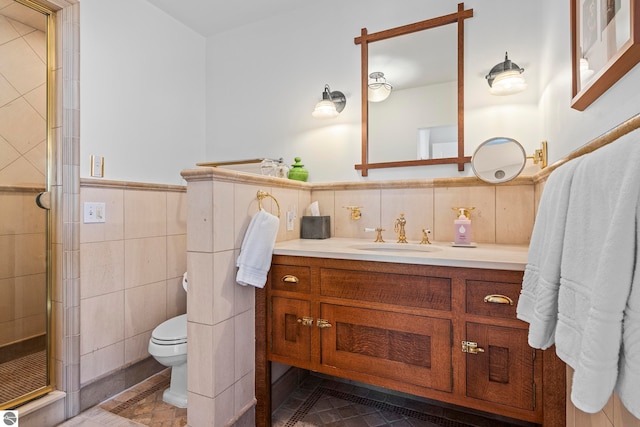full bath featuring a stall shower, wainscoting, vanity, tile walls, and toilet