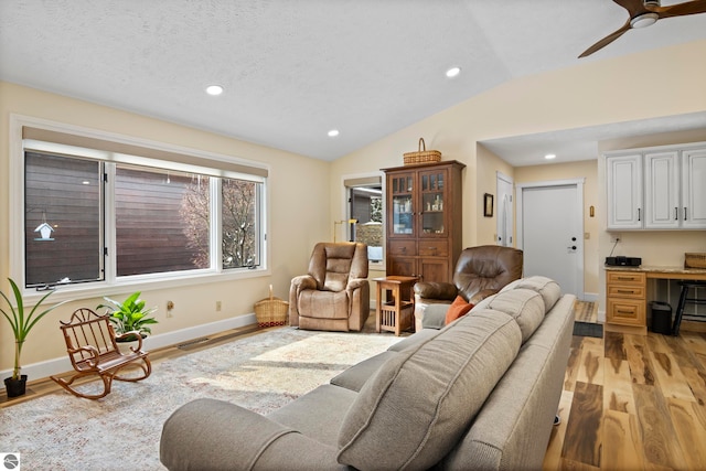 living room with lofted ceiling, light wood-type flooring, a textured ceiling, ceiling fan, and built in desk