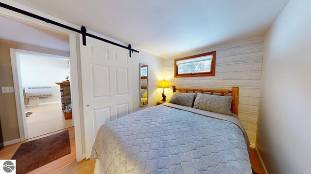 bedroom with light wood finished floors, radiator, a barn door, and wood walls