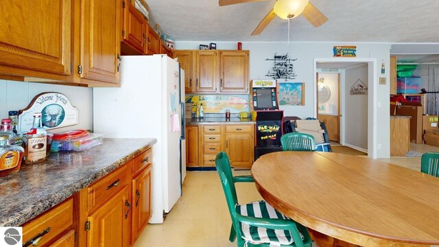 kitchen featuring brown cabinets, ceiling fan, light floors, and freestanding refrigerator