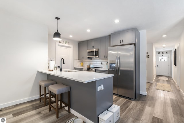 kitchen featuring kitchen peninsula, hanging light fixtures, appliances with stainless steel finishes, hardwood / wood-style floors, and decorative backsplash