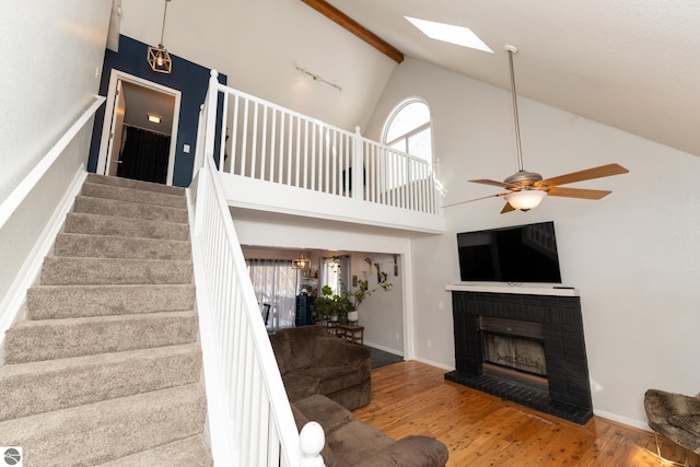 living room with a fireplace, high vaulted ceiling, ceiling fan, a skylight, and hardwood / wood-style floors