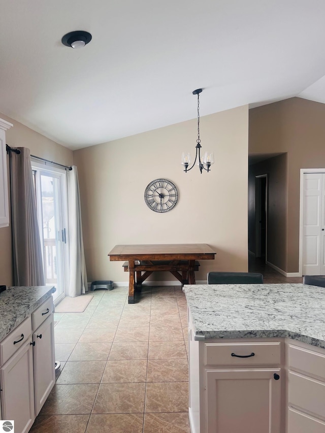 kitchen featuring decorative light fixtures, light stone counters, white cabinets, and lofted ceiling