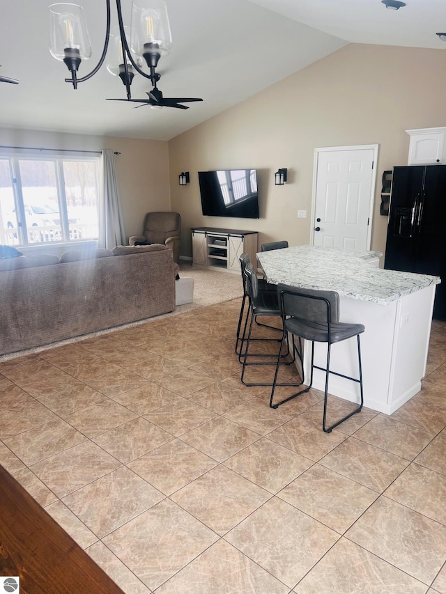 kitchen with light stone countertops, white cabinets, black fridge with ice dispenser, a center island, and a kitchen bar