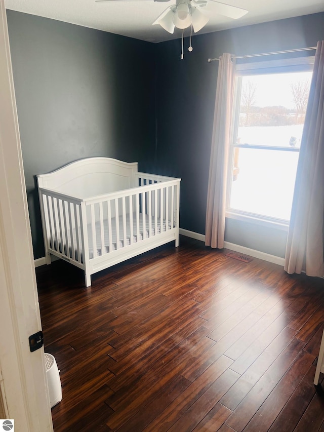 unfurnished bedroom with ceiling fan, dark hardwood / wood-style floors, and a nursery area