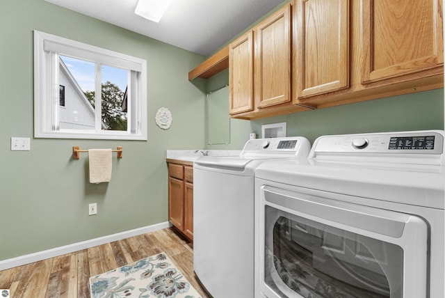 laundry area featuring sink, washing machine and clothes dryer, light hardwood / wood-style floors, and cabinets