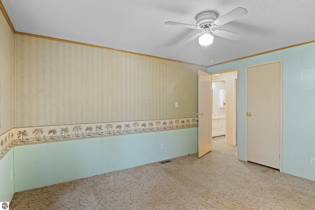 spare room with a textured ceiling, light carpet, crown molding, and ceiling fan