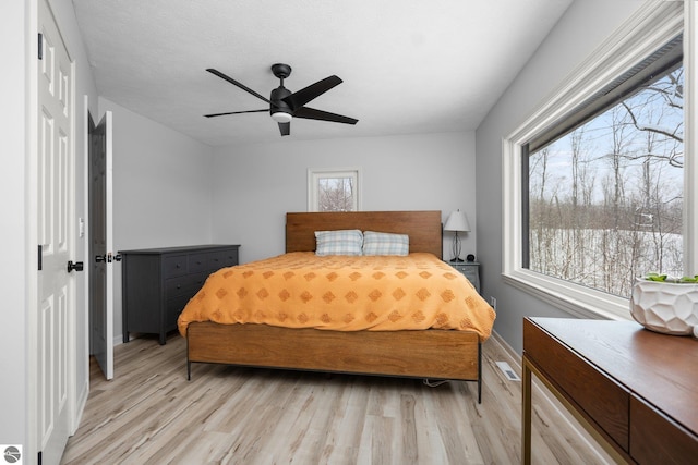 bedroom with ceiling fan, multiple windows, and light hardwood / wood-style flooring