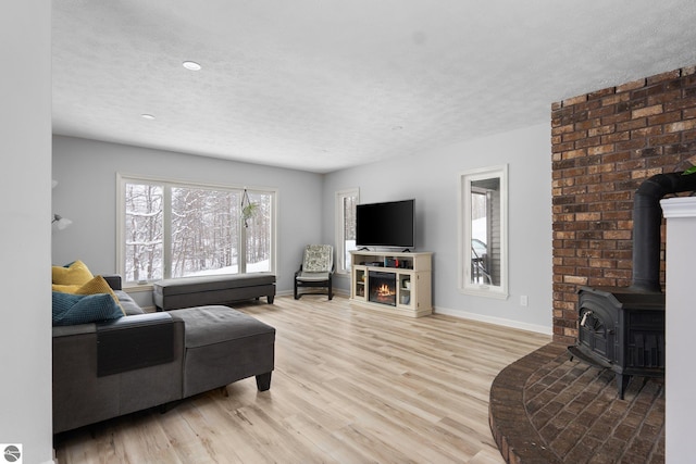 living room featuring a textured ceiling, a wood stove, a fireplace, and light hardwood / wood-style flooring