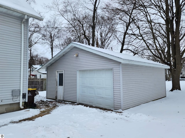 snow covered garage featuring a detached garage and fence