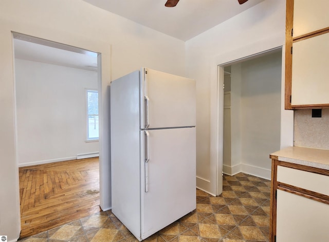 kitchen featuring ceiling fan, a baseboard heating unit, baseboards, light countertops, and freestanding refrigerator