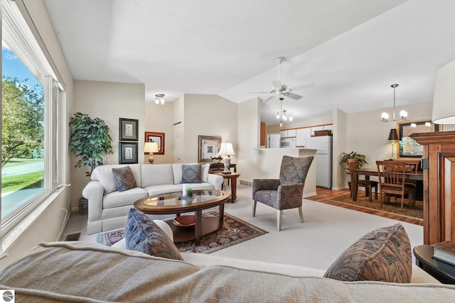 living room featuring lofted ceiling, light wood-style flooring, a wealth of natural light, and ceiling fan with notable chandelier