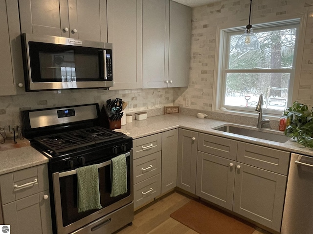 kitchen with tasteful backsplash, light wood-style flooring, appliances with stainless steel finishes, decorative light fixtures, and a sink