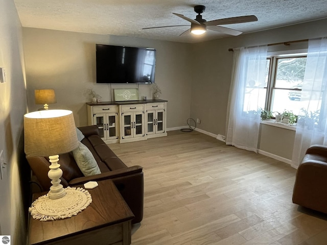 living room featuring light wood finished floors, ceiling fan, baseboards, and a textured ceiling