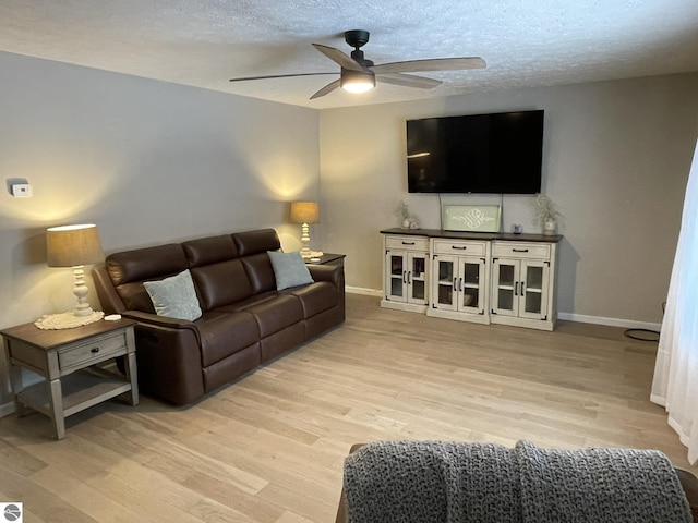 living room with a ceiling fan, light wood-type flooring, a textured ceiling, and baseboards