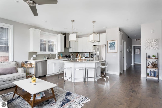 kitchen featuring stainless steel appliances, a kitchen island, light countertops, wall chimney range hood, and decorative light fixtures