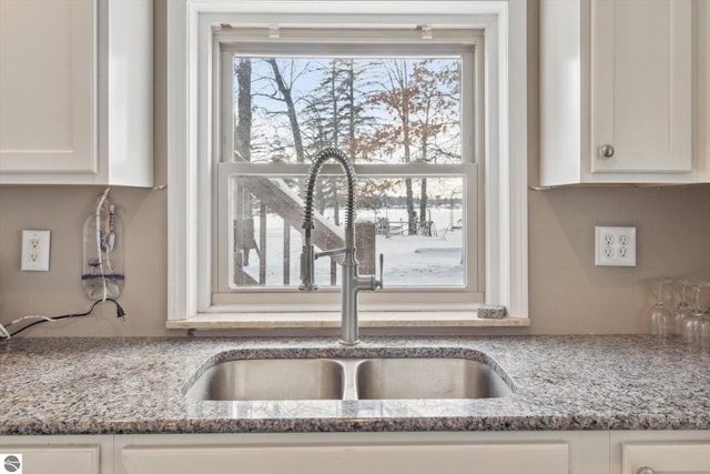 kitchen with light stone counters, white cabinets, and a sink